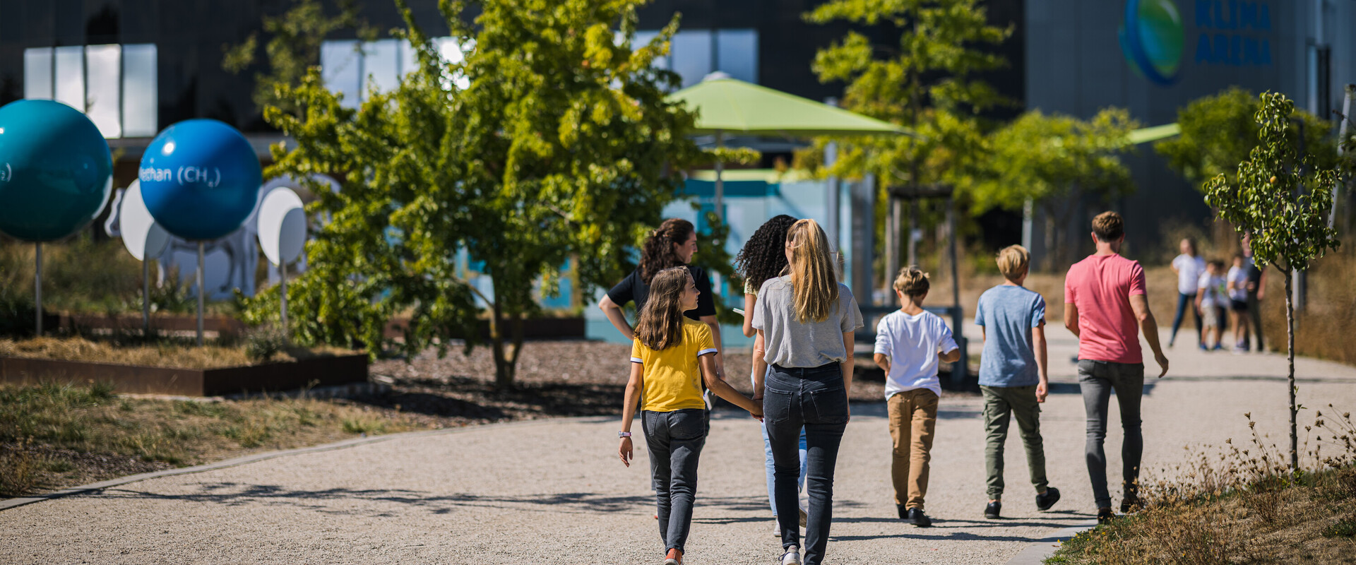 Famile l&auml;uft durch die Au&szlig;enanlage auf das Geb&auml;ude der KLIMA ARENA zu.